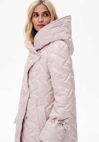 Puchowy, jasnoróżowy płaszcz z dużym, usztywnionym kapturem, o fakturze w romby, ze ściąganymi rękawami, z bocznymi kieszeniami i zapięciem na guziki.