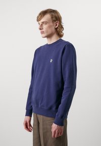 Felpa blu navy in cotone, con colletto a girocollo a coste, maniche lunghe e un piccolo logo sul petto sinistro. Texture liscia.