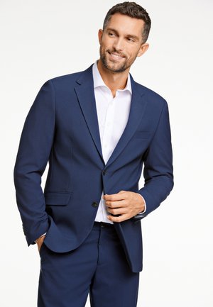 Marineblaues Anzug mit einreihiger Jacke, Reverskragen und zwei Taschen. Kombiniert mit einem weißen Hemd und dunklen Hosen.
