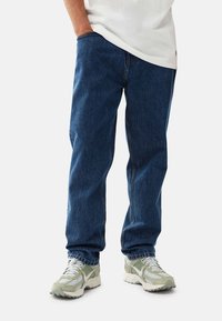 Blå denimjeans med rak benlängd, med en klassisk femfickdesign. Bärs med ljusgröna sneakers och en vit skjorta.