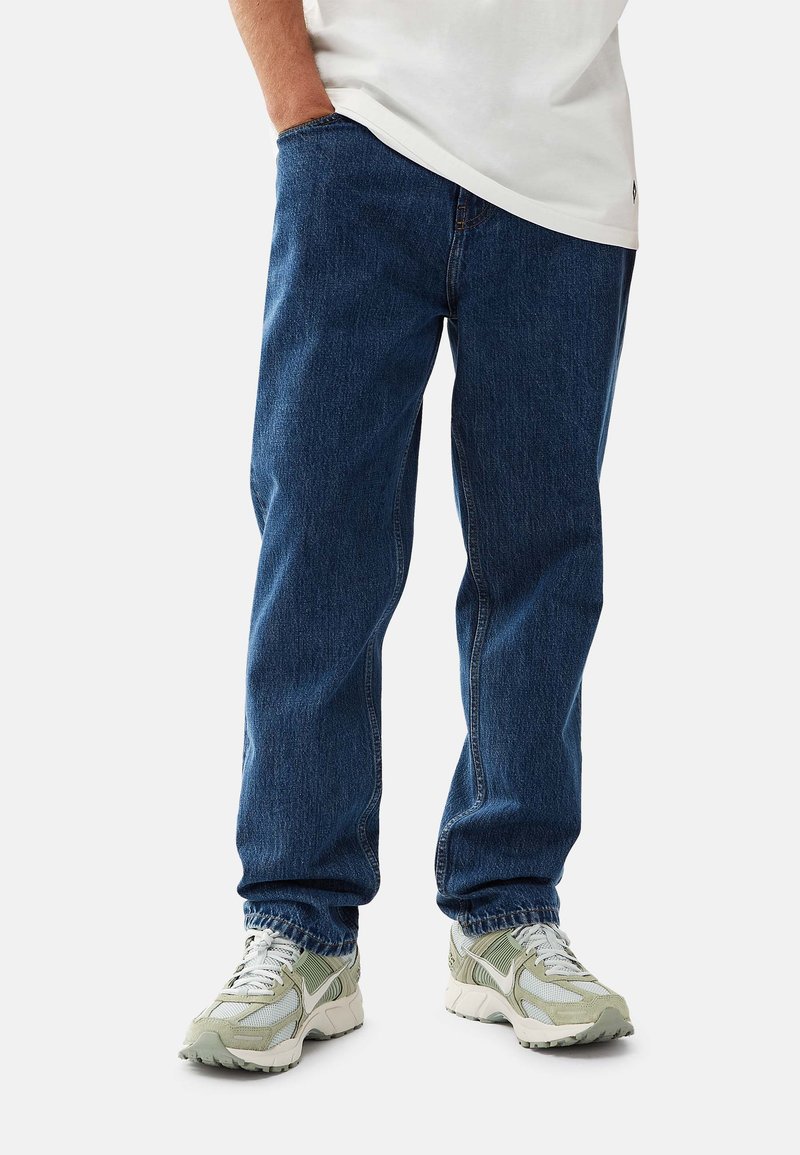 Blå denimjeans med rak benlängd, med en klassisk femfickdesign. Bärs med ljusgröna sneakers och en vit skjorta.