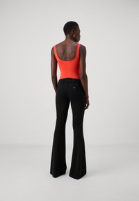 Body arancione brillante senza maniche abbinato a pantaloni neri a palazzo. Il body presenta una schiena bassa e i pantaloni hanno un sottile dettaglio con logo.