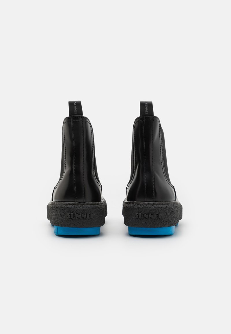 Stivali alla caviglia neri in pelle con suola nera texturizzata e dettagli blu. Presentano un linguetta per il tallone e cuciture minime sul retro.