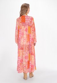 Abito maxi in vivaci motivi patchwork rosa, arancione e giallo. Maniche lunghe e fluttuanti con una vestibilità ampia e un tessuto leggero e strutturato.