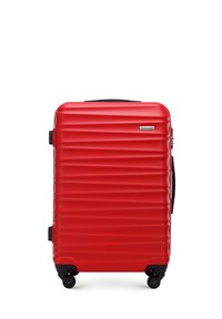 Red hard-shell suitcase with textured ridges, black zip, side handle, and four swivel wheels for mobility. Brand logo on the front.