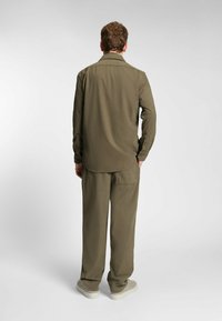 Olijfgroene, relaxed-fit shirt en broek van lichte stof, met een button-down kraag en lange mouwen, gecombineerd met lichte schoenen.