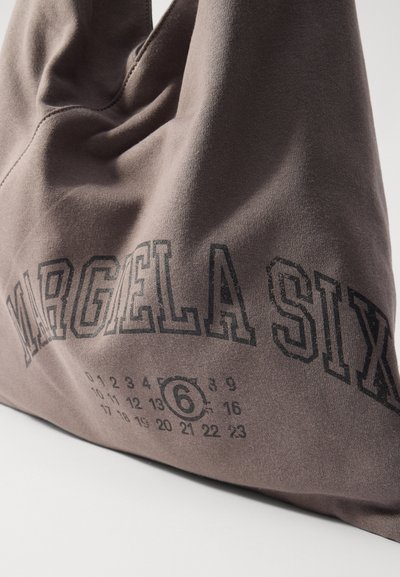 Sac fourre-tout en tissu brun avec "MARGELA SIX" en lettres noires en gras et un motif de calendrier avec le numéro 6 en surbrillance en bas.