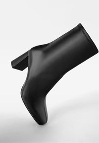 Schwarzer Leder-Stiefelette mit quadratischem Absatz. Glatte Textur, eng anliegendes Design und saubere Nähte entlang der oberen Kante.