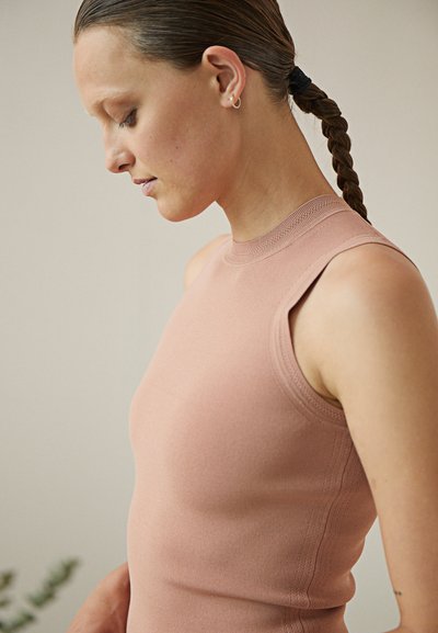 Απαλή ροζ χωρίς μανίκια μπλούζα από ριμπ ύφασμα, με ψηλό λαιμό και εφαρμοστή σχεδίαση, συνοδευόμενη από λεπτές ραφές.