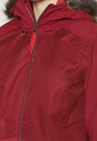 Czerwona ocieplana kurtka z teksturowanym wykończeniem, z zamkiem błyskawicznym z przodu oraz kapturem ozdobionym futrzanym wykończeniem.