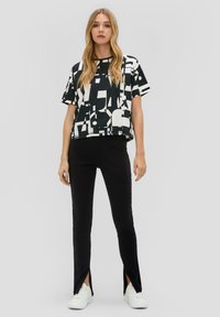 Haut à manches courtes noir et blanc à motif avec une silhouette carrée, associé à un pantalon noir ajusté avec des ourlets fendus sur les côtés, porté avec des baskets blanches.