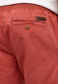 Røde bomullsshorts med en baklomme med knappelukking og et merket lærpatch, som viser et enkelt og uformelt design.