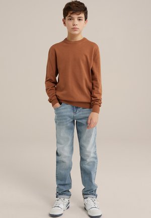 Maglione a maglia marrone, jeans azzurri chiari e sneakers bianche con dettagli neri. Vestibilità dritta, maniche lunghe, design semplice a girocollo.
