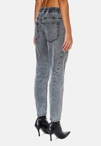 Pantalones de mezclilla grises con cintura elástica, corte holgado y dos bolsillos traseros. Combinados con botines negros puntiagudos.