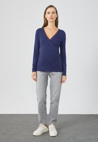 Ναυτικό μπλουζάκι με μακριά μανίκια, V- λαιμόκοψη και δαντέλα, συνδυασμένο με ανοιχτό γκρι τζιν ίσιας γραμμής και λευκά αθλητικά παπούτσια. Απλός και εφαρμοστός σχεδιασμός.