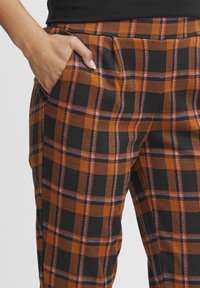 Plaid pants in orange, black, and purple. Features a relaxed fit, side pocket, and textured fabric with a bold check pattern.
