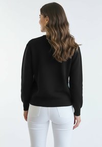 Czarny dziergany sweter z prążkowanym kołnierzem i mankietami, o luźnym kroju. Połączony z białymi jeansami o dopasowanym kroju, ukazującymi gładką fakturę.