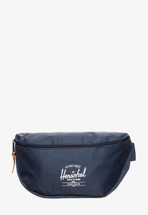 Marineblauwe Herschel Supply Co. heuptas met rits, wit logo aan de voorkant en leren ritstrekker.