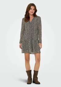 Musthave mustrisidega mustriga kleit pika varrukaga ja nupuga esiosas, millel on kihiline, voogav disain ja pehme, kerge kangas. Pruunid põlvekõrgused saapad.