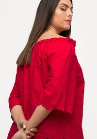Rode geborduurde blouse met een geschulpte off-the-shoulder halslijn. Heeft bloemenpatronen en driekwart mouwen.