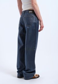 Avslappnat passform mörkblå denimjeans med hög midja och vida ben. Har bakfickor och en märkesetikett vid midjebandet.