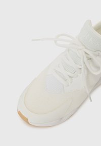 Hvit atletisk sko med mesh-overdel, lyse grønne detaljer, flate snører og såle av gummigummi, med et slankt, moderne design.