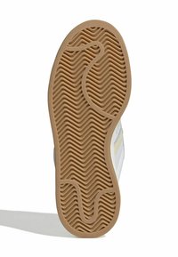 Rubber outsole with a zigzag tread pattern, featuring a textured beige surface. Predator foam accents on a white upper provide grip and support.