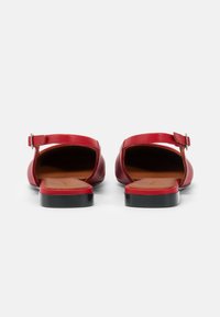 Sandales en cuir rouge avec un dos fermé, une sangle à la cheville et une boucle, semelle noire plate et côtés ouverts mettant en valeur des semelles intérieures beige.