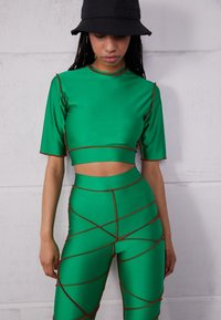 Conjunto de duas peças verde, feito de material suave, apresentando um top cropped e leggings de cintura alta com costura vermelha e um design geométrico.