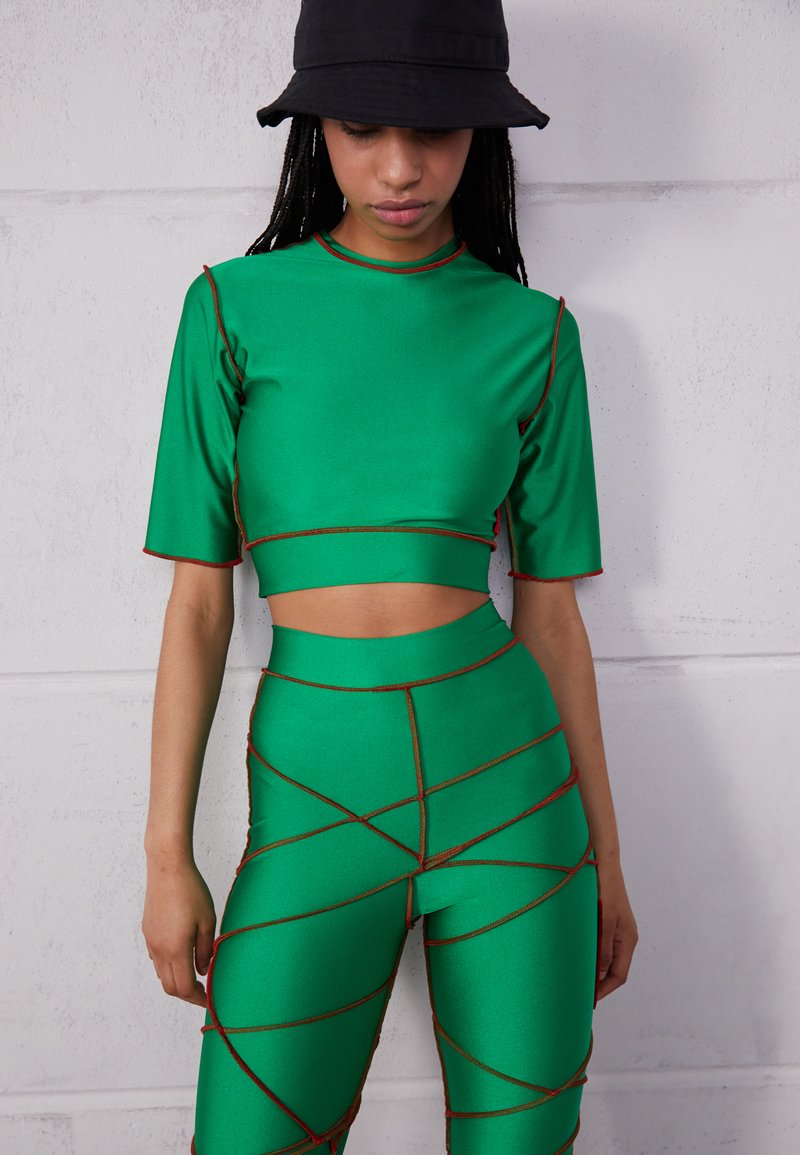 Conjunto de duas peças verde, feito de material suave, apresentando um top cropped e leggings de cintura alta com costura vermelha e um design geométrico.