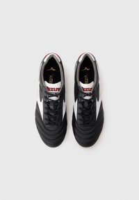Pantofi de fotbal alb-negru cu un design texturat, având vârf rotund, sireturi și accente roșii pe limbă și pe laterale.