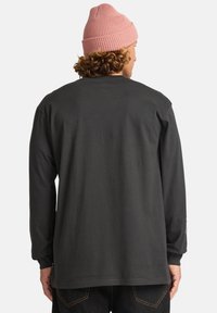 Dunkelgraues Langarmhemd mit lässiger Passform, aus Baumwollmaterial und mit gerippten Bündchen. Getragen mit einer hellrosa Strickmütze.
