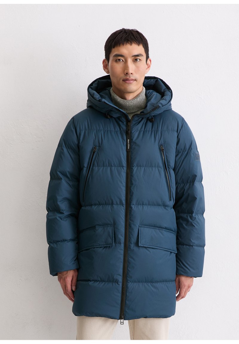 Manteau matelassé bleu marine avec capuche, présentant des panneaux matelassés, des poches poitrine zippées et une fermeture éclair frontale. Tissu texturé et coupe décontractée.