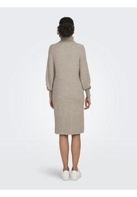 Abito lavorato a maglia beige con colletto alto, maniche lunghe e silhouette dritta, che arriva a metà polpaccio. Il tessuto sembra morbido e strutturato.