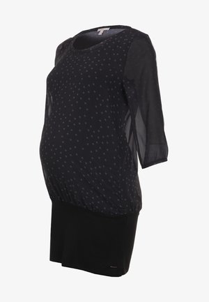 Sort graviditetskjole med gennemsigtige trekvartlange ærmer og lille gentaget hvidt blomsterprint på den øverste halvdel.