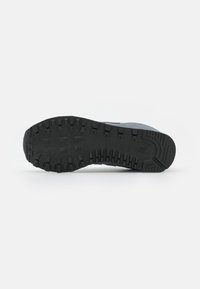 Suola in gomma nera di una scarpa con battistrada profondo per una buona aderenza. Presenta un design testurizzato con un logo in rilievo verso il tallone.