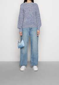 Jasnoniebieski sweter o teksturowanym wzorze z balonowymi rękawami, w połączeniu z jasnoniebieskimi spodniami typu wide-leg i małą niebieską torebką. Białe sneakersy dopełniają całość.