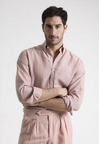 Camisa de rayas rosa claro con detalles de botones, puños enrollados y collar, combinada con pantalones rosa claro de corte tailored con un botón lateral.