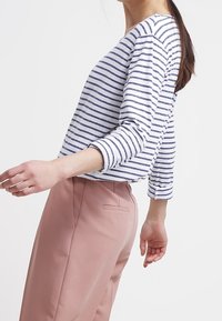 Maglietta a maniche lunghe a righe bianca e blu navy, abbinata a pantaloni rosa. La maglietta presenta una vestibilità morbida e un ampio scollo, evidenziando le righe.