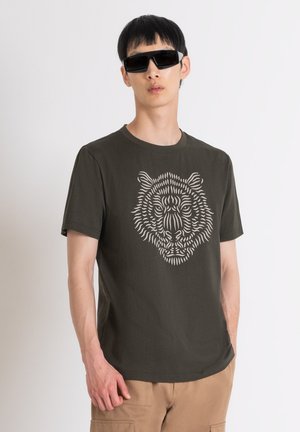 Camiseta verde oliva con un gráfico de tigre blanco, de manga corta, cuello redondo, hecha de algodón, llevada con gafas de sol negras y pantalones beige.