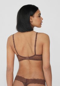 Soutien-gorge en dentelle marron et string assorti avec des bretelles réglables et fermeture à crochets; détails en texture transparente sur le tissu.
