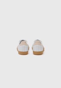 Baskets en cuir blanc avec un accent beige au talon et une semelle en caoutchouc gomme. Elles présentent un col rembourré et des détails arrière texturés.