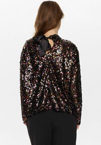 Top in paillettes nere con un fiocco di raso nero legato sul retro, caratterizzato da paillettes multicolori lucide su un tessuto trasparente, design morbido.