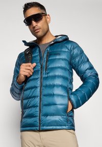 Μπλέ φουσκωτό μπουφάν με φερμουάρ μπροστά, πλαϊνές τσέπες και κουκούλα. Διαθέτει λογότυπο Columbia στο στήθος και αντίθετες γκρίζες λεπτομέρειες.