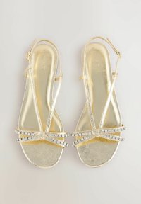 Guld sandaler med en glänsande metallisk finish, med tunna remmar och rhinestone-dekorationer över framsidan och vristen för säker förslutning.