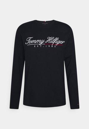Long-sleeve black t-shirt made of cotton, featuring white and red embroidered "Tommy Hilfiger" logo and "EST. 1985" detail. Round neckline.