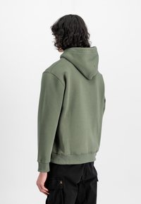 Grüne Baumwollkapuzenjacke mit einer Kängurutasche, gerippten Bündchen und einer verstellbaren Kapuze. Die Rückansicht zeigt eine bequeme Passform.