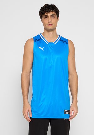 Młody mężczyzna w jaskrawo niebieskiej, bezrękawnikowej koszulce sportowej Puma z ciemnoniebieskimi zygzakowatymi detalami przy ramionach.