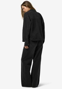 Svart denimjakke og vide bukser, med en avslappet passform, myk tekstur, sømdetaljer og subtile lommer i en ensfarget farge.