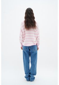 Sweatshirt rayé rose et blanc, coupe oversize, texture douce, associé à un jean bleu taille haute, affichant un style denim classique.